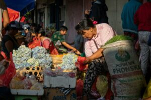 A bustling street market scene with local vendors selling fresh produce and flowers in an urban setting.