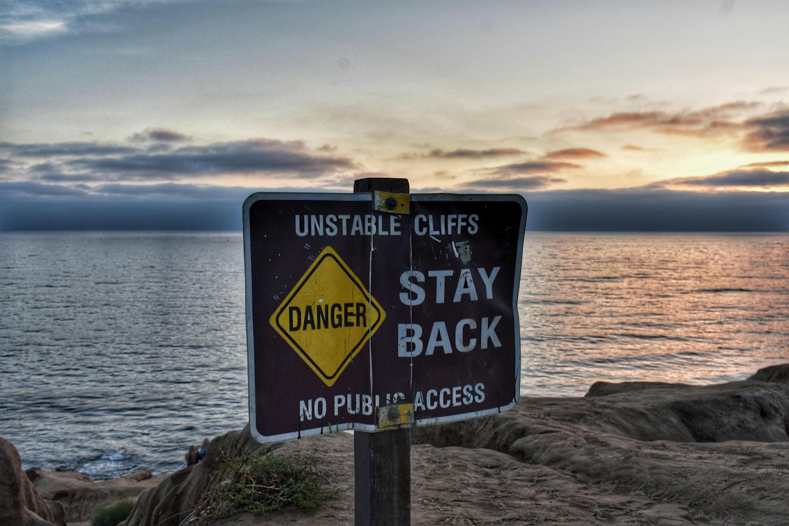 A warning sign on unstable cliffs at sunset by the ocean, capturing a scenic coastal landscape.